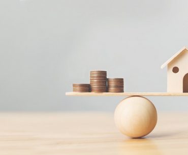 Wooden home and money coins stack on wood scale.