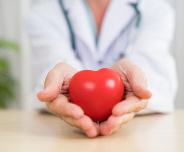 Unrecognizable doctor holding red heart shape in hands.