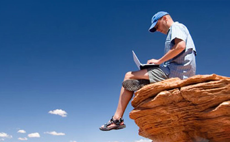 Man working on laptop sitting on edge of rocky outcrop